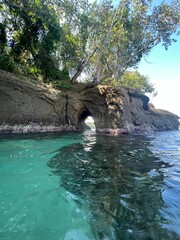Fototapeta premium Serene view of a natural rock arch framed by lush greenery, showcasing tranquil turquoise waters. Ideal for travel and nature themes, evoking a sense of adventure.
