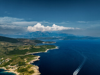 View of Rocky Shore Covered with Greenery on the Adriatic Coast with Epic Clouds and Mountains in the Background