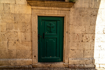 old wooden green door in stone buliding with cross on it