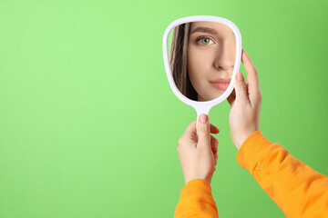 Beautiful woman looking in handheld mirror on green background, closeup. Space for text