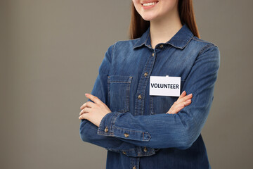 Volunteer with badge on grey background, closeup. Space for text