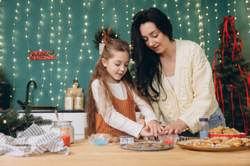Mother and daughter baking christmas cookies together in decorated kitchen