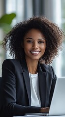 With a radiant smile and focused demeanor, a black businesswoman engages in her work at a sleek desk in an airy office, showcasing professionalism and positivity