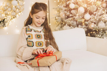 Girl opening christmas gift on sofa near decorated tree