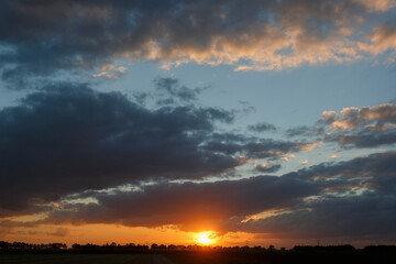 Fototapeta premium Vibrant sunset casts colorful hues over a tranquil landscape with an expansive sky filled with clouds