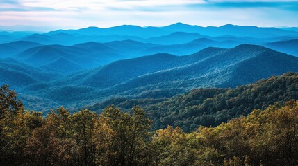 Obraz premium Panoramic view of layered blue mountains under a partly cloudy sky, autumn foliage in the foreground.