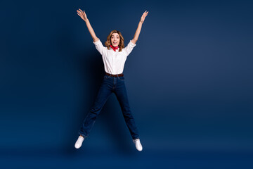 Obraz premium Young woman joyfully jumping against a dark blue background wearing stylish casual outfit