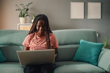 Obraz premium Young woman working from home using laptop on the sofa