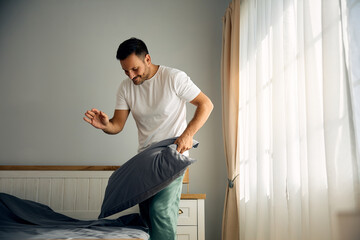 Happy man making his bed in  morning.