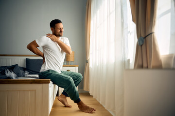 Mid adult man holding his back and shoulder in pain after waking up in morning.