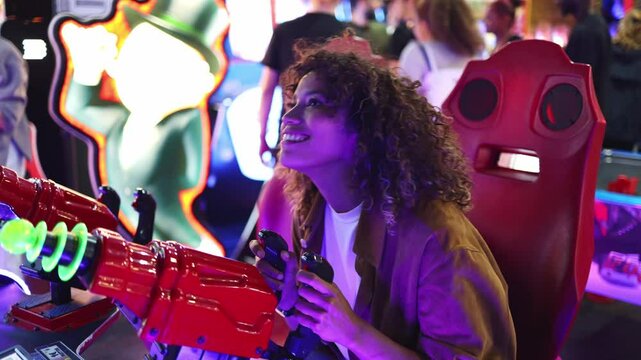 Latin woman with curly hair enjoys playing an arcade shooting game, surrounded by colorful lights and a vibrant atmosphere