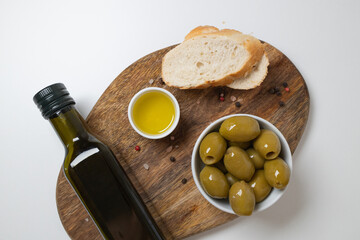 Organic Olive Oil in bowl with green olives and ciabatta bread on white background ,top view, copy...