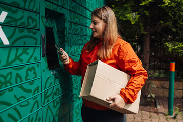 Caucasian woman picks up parcel from automatic post office machine, standing with phone near the...