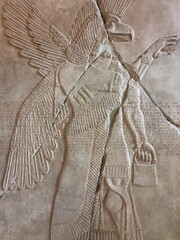 A vertical close-up of a wall relief with a winged Mesopotamian eagle god, Apkallu or Abgal, in an...