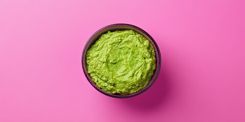 Obraz premium A vibrant pink background provides a striking contrast to a bowl of creamy, freshly made guacamole, highlighting its rich green hue and smooth texture.