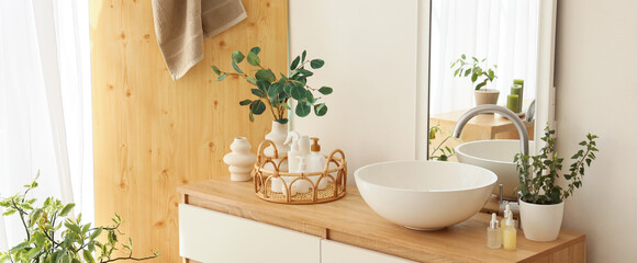 Vase with eucalyptus, cosmetic products and sink on commode in bathroom