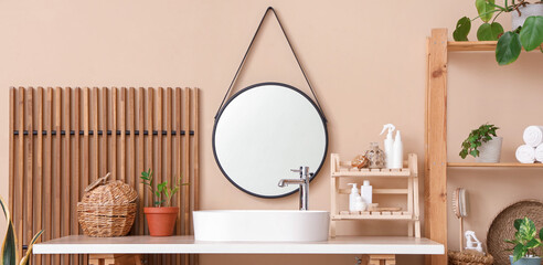 Modern sink, table and shelving unit near beige wall in interior of bathroom