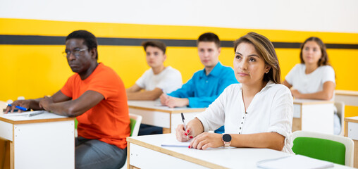 Latin woman listening to lecture in taxi training school with group of people.