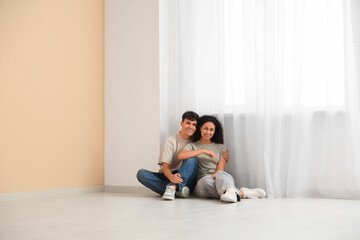 Fototapeta premium Happy young couple sitting on floor in empty room, new home ownership and relocation concept, real estate investment