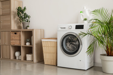 Interior of light laundry room with washing machine, basket and shelf unit