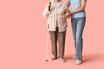 Young woman with blind grandmother on pink background
