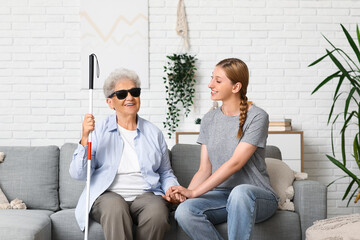 Young woman with blind grandmother holding hands on sofa at home