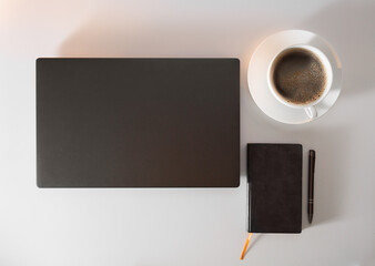 On the table there is a laptop, a notepad, a pen and a cup of coffee with foam