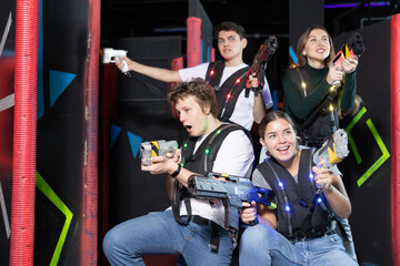 Positive girls and guys playing laser tag game opposite each other in modern dark room