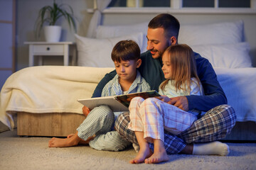 Father reading bedtime story to his children in bedroom