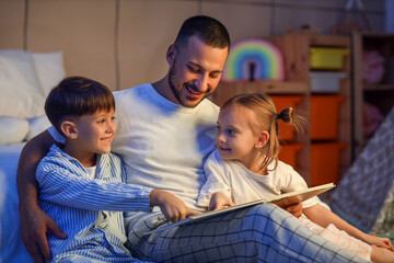 Happy father and his cute little children reading bedtime story at home
