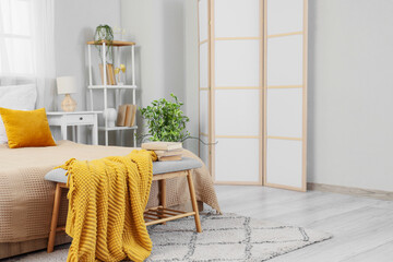 Interior of stylish bedroom with folding screen and yellow plaid on soft bench