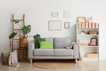 Obraz premium Comfortable sofa, shelving unit and Monstera houseplant in interior of living room