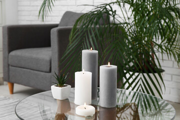 Burning candles with plant on table in living room, closeup