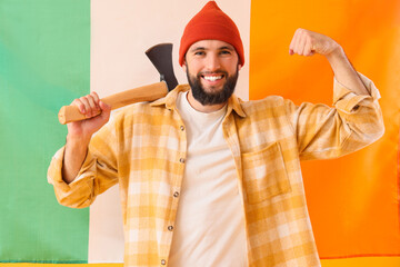 Handsome lumberjack with axe showing muscles against flag of Ireland