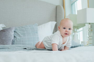 Happy baby. Cute little newborn girl with smiling face crawling on bed in bedroom. Infant baby...