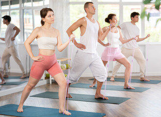 Fototapeta premium Sporty woman taking part in intense group training in gym exercising with resistance band, strong biceps or abs muscles in gym health center