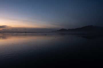 Beach at dusk, with reflections and light clouds in the distance