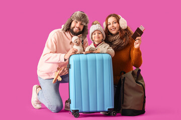 Happy family in winter clothes with toys and suitcase on violet background. Travel concept