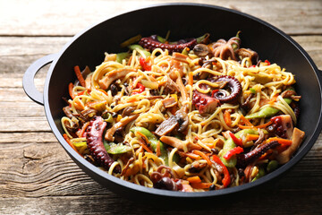 Stir-fry noodles with sea food and vegetables in wok on wooden table, closeup