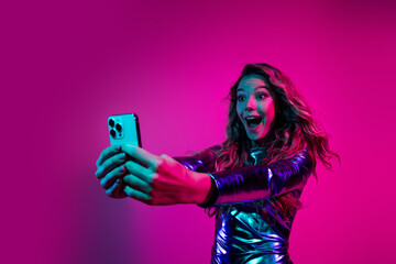 Energetic woman taking a selfie in a shiny blue dress on a vibrant pink backdrop, expressing excitement and joy at a disco celebration