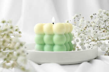Stylish bubble candle and gypsophila flowers on white cloth, closeup