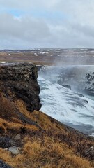 Picturesque Gullfoss cascade in nordic region within icelandic nature presenting breathtaking scenery with frost covered meadows and frozen water running down hills. Northern beauty on hillside.