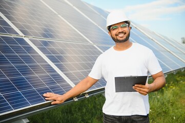 An Indian male engineer working on a field of solar panels. The concept of renewable energy