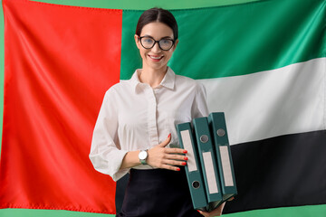 Young businesswoman with folders against UAE flag on green background