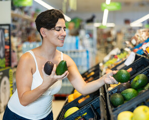 Portrait of cheerful female buyer taking fresh ripe avocado on the supermarket