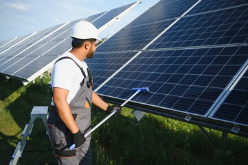 Professional indian worker cleans solar panels with brush, green electric power technology