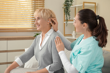 Doctor putting hearing aid on mature woman's ear while visiting her at home
