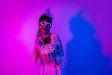 Young woman in elegant lace dress enjoying popcorn under neon lights at vibrant masquerade party
