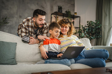 Mum, dad and son watch cartoon or movie on laptop and sit on sofa