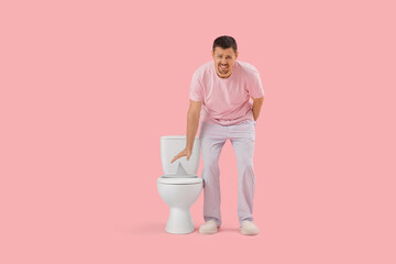 Suffering man near toilet bowl with paper pin on pink background. Hemorrhoid concept
